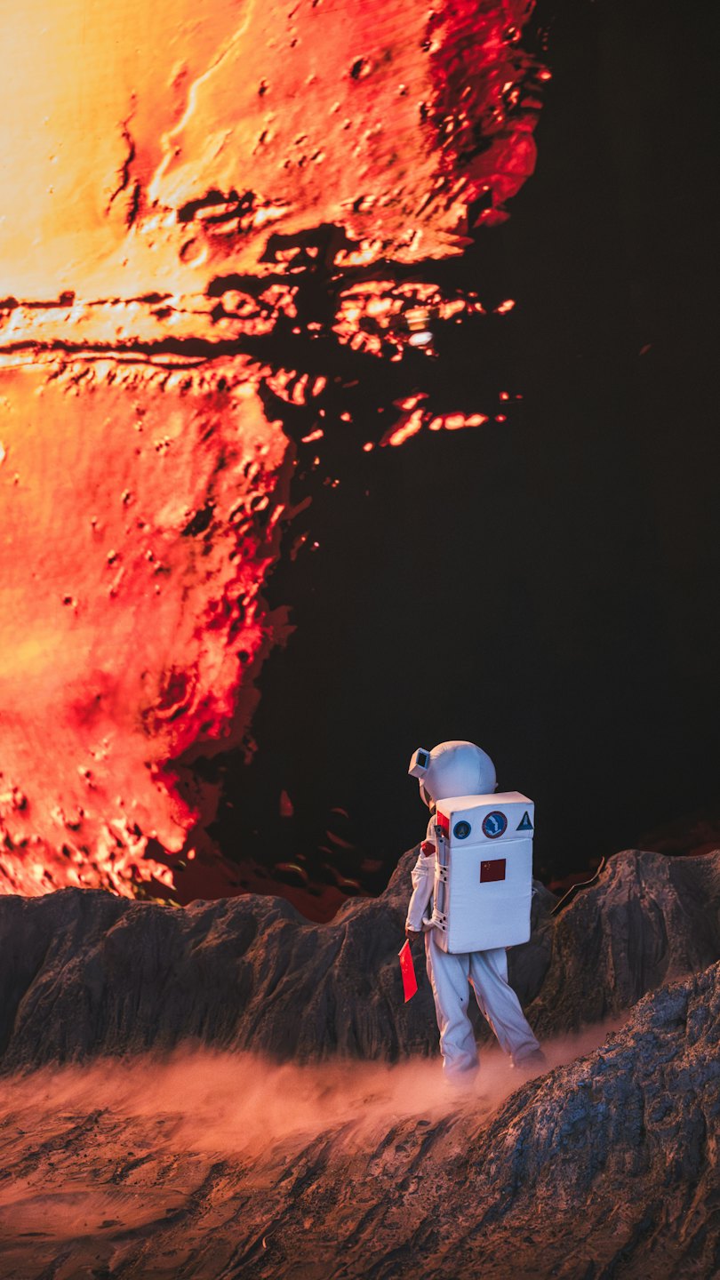 An astronaut standing on rocky alien terrain viewing a planet.